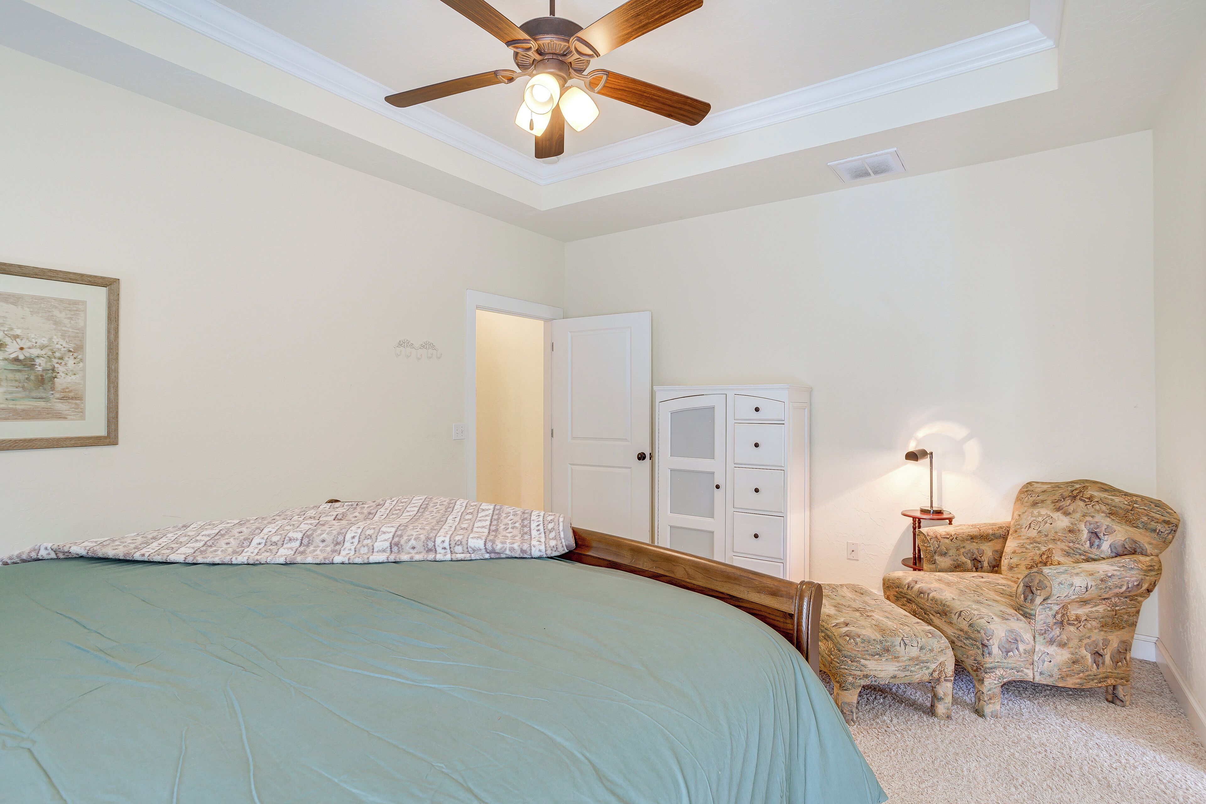 A bedroom with a bed, a chair, a ceiling fan, and a door.