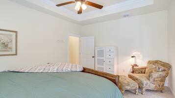 A bedroom with a bed, a chair, a ceiling fan, and a door.
