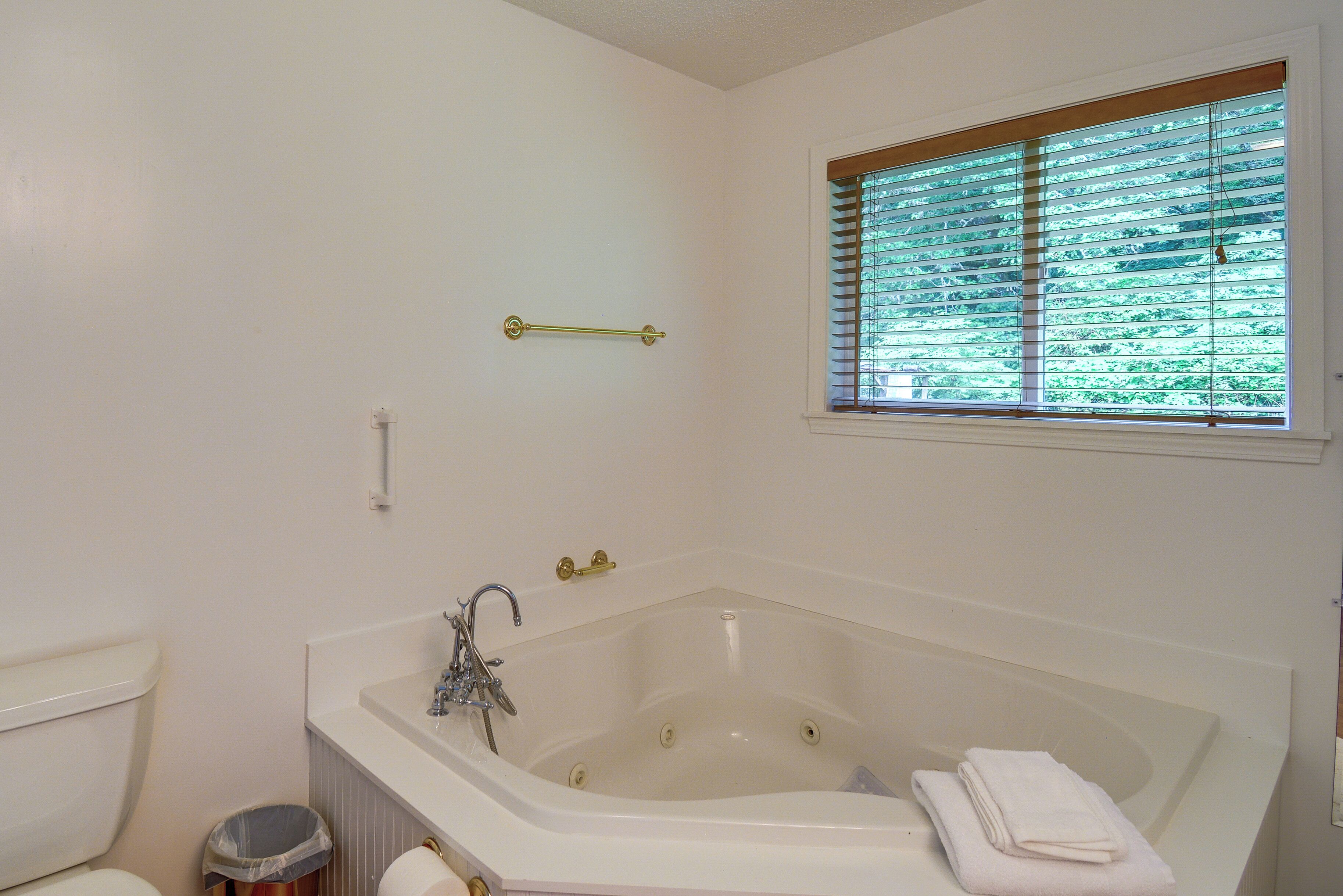 A bathroom with a bathtub, toilet, and window with blinds.