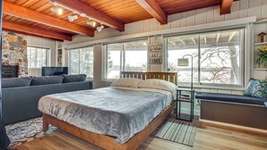 Une chambre avec un lit en bois, un canapé gris, une cheminée en pierre et de grandes fenêtres.