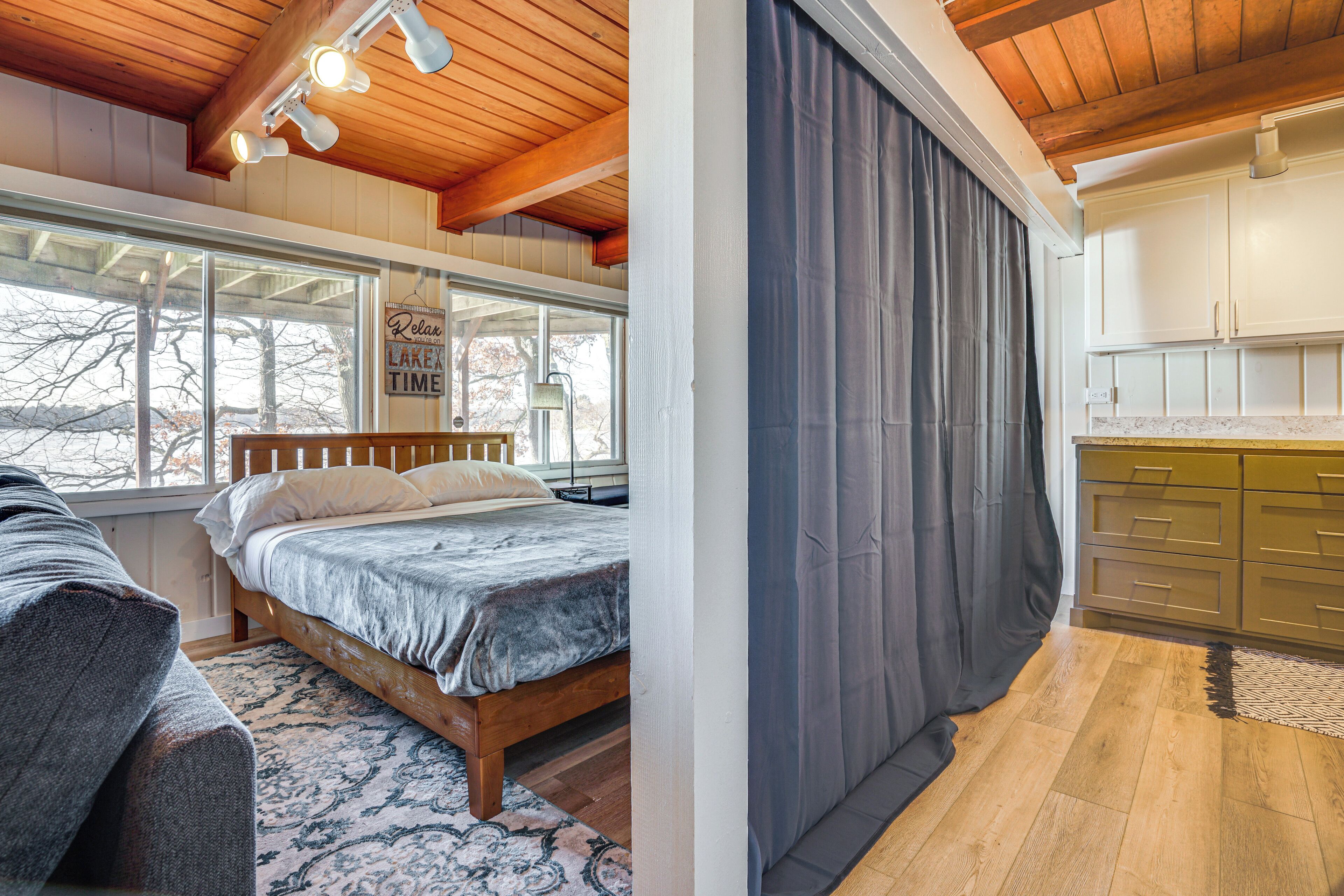 Ein Schlafzimmer mit einem großen Bett, einem Fenster und Blick auf Bäume. Das Zimmer hat Holzbalken an der Decke und ein Fenster mit Blick ins Grüne.