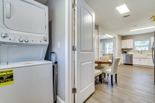 A laundry area with a front-loading washer and dryer, a dining area with a table and chairs, and a kitchen with white cabinets and a dishwasher.