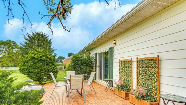 Eine Holzterrasse mit Gartenmöbeln, ein Holzpflanzgefäß mit Blumen und Blick auf eine grüne Landschaft.