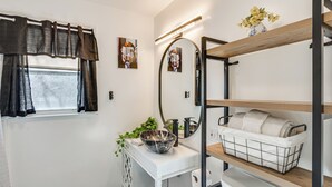 Ein kleines Badezimmer mit einem weißen Waschtisch, einem großen Spiegel, einer schwarzen Waschschüssel und einem Regal mit Handtüchern.
