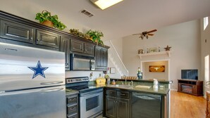 A modern kitchen with a built-in refrigerator, stove, microwave, and dishwasher. There is a staircase leading to a second floor, and a television in the corner.