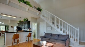 A spacious living area with a wooden floor, a gray sofa, a coffee table, and a staircase with white railings.