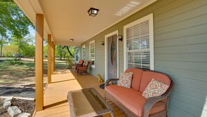 A covered porch with a wicker sofa and chairs, a small table, and a dog.