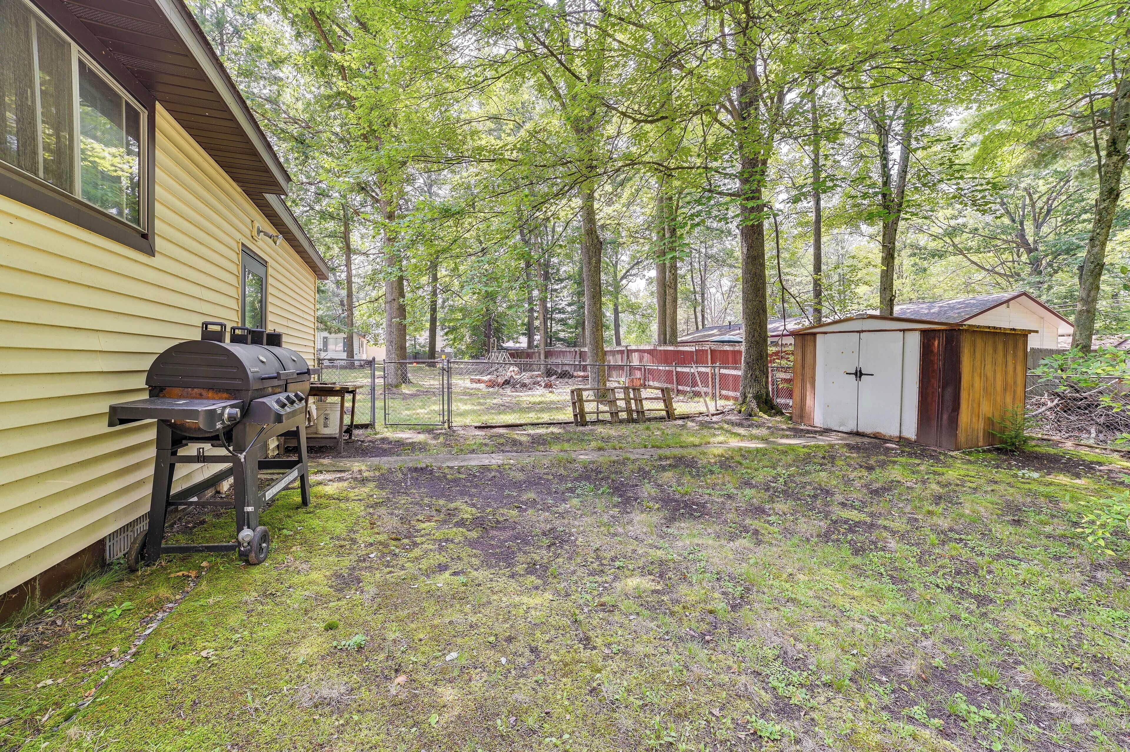 Ein Garten mit Grill, Gartenhaus und einer Holzterrasse.