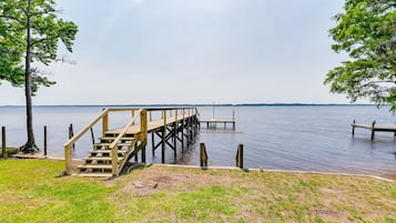 A wooden pier extending into calm water, surrounded by grassy areas and trees.