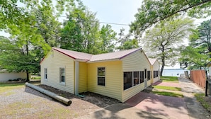 A yellow single-story house with a red roof, a front porch, and a view of a lake.