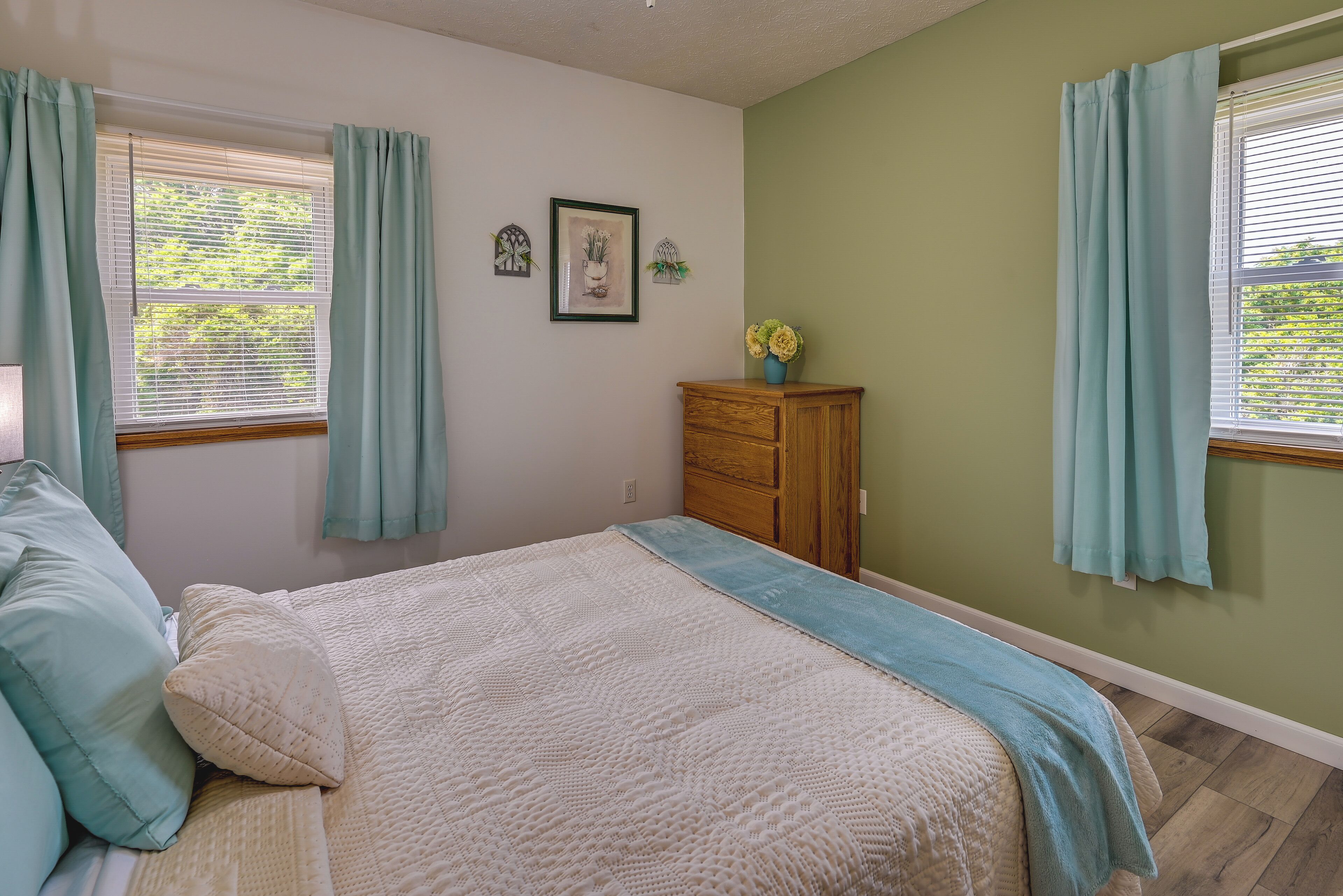 A bedroom with a bed, a dresser, and a window with curtains.