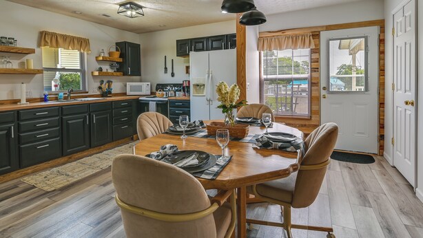 A dining area with a wooden table set for four, surrounded by dark cabinets and a kitchen in the background. - Charming Smiths Grove Home Near Cave Tours! (Smiths Grove)