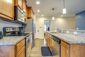 A modern kitchen with granite countertops, wooden cabinets, stainless steel appliances, and pendant lighting.