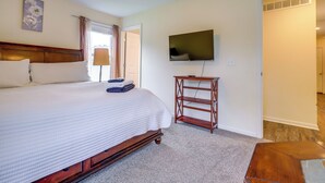 A bedroom with a large bed, a television on the wall, and a wooden nightstand. - Covered Balcony! Family-friendly Lansing Home (Lansing)