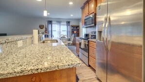 A kitchen with granite countertops, stainless steel appliances, wooden cabinets, and pendant lighting. - Covered Balcony! Family-friendly Lansing Home (Lansing)