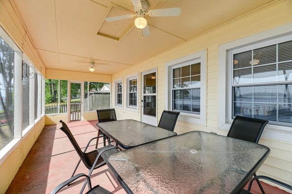 A covered patio with a glass table and chairs, large windows, and a ceiling fan. - Riverfront Edenton Condo w/ Porch & Water Views! (Edenton)