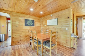 A wooden-paneled room with a wooden dining table and chairs, a framed sign on the wall, and a small shelf with items.
