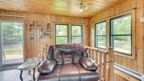 A wooden cabin interior with a leather sofa, large windows, and a wooden deck. - Lakefront Wisconsin Home - Deck, Fire Pit & Kayaks (Stone Lake)