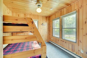 A wooden cabin with a bunk bed, large windows, and a ceiling fan.