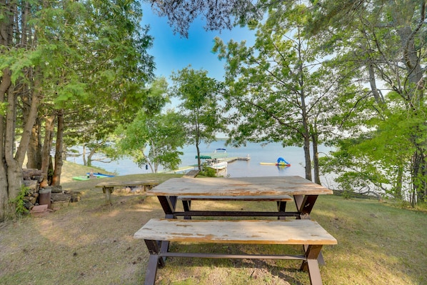A picnic table in a wooded area with a lake and boats in the background.
