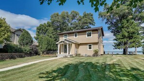 Una casa de dues plantes amb un porxo, un jard í ben cuidat i vista a un llac.