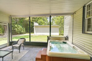 A covered patio with a hot tub, a chair, and a view of the backyard.