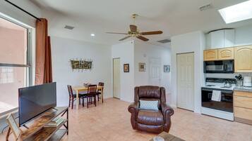 A modern living room with a flat-screen TV, a leather armchair, a dining table with chairs, and a kitchen area with a microwave and stove.