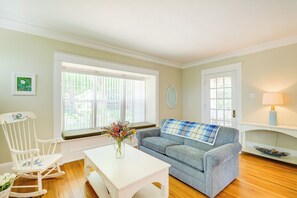 Uma sala de estar com um sofá azul, uma cadeira de balanço branca e uma mesa de centro branca.