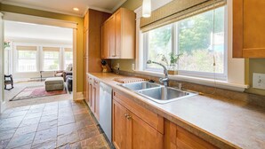 A spacious kitchen with wooden cabinets, a double sink, and a large window with a view of greenery. - Cozy Michigan Retreat w/ Deck & Gas Grill! (Frankfort)