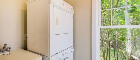 A compact laundry area with a washing machine and dryer stacked on top of each other, a sink, and a window with a view of greenery.