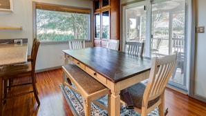 Un comedor con mesa y sillas de madera, un banco y vistas a una terraza exterior a través de un ventanal corredero.