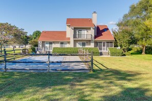 A two-story house with a red roof, a balcony on the second floor, and a fenced backyard.