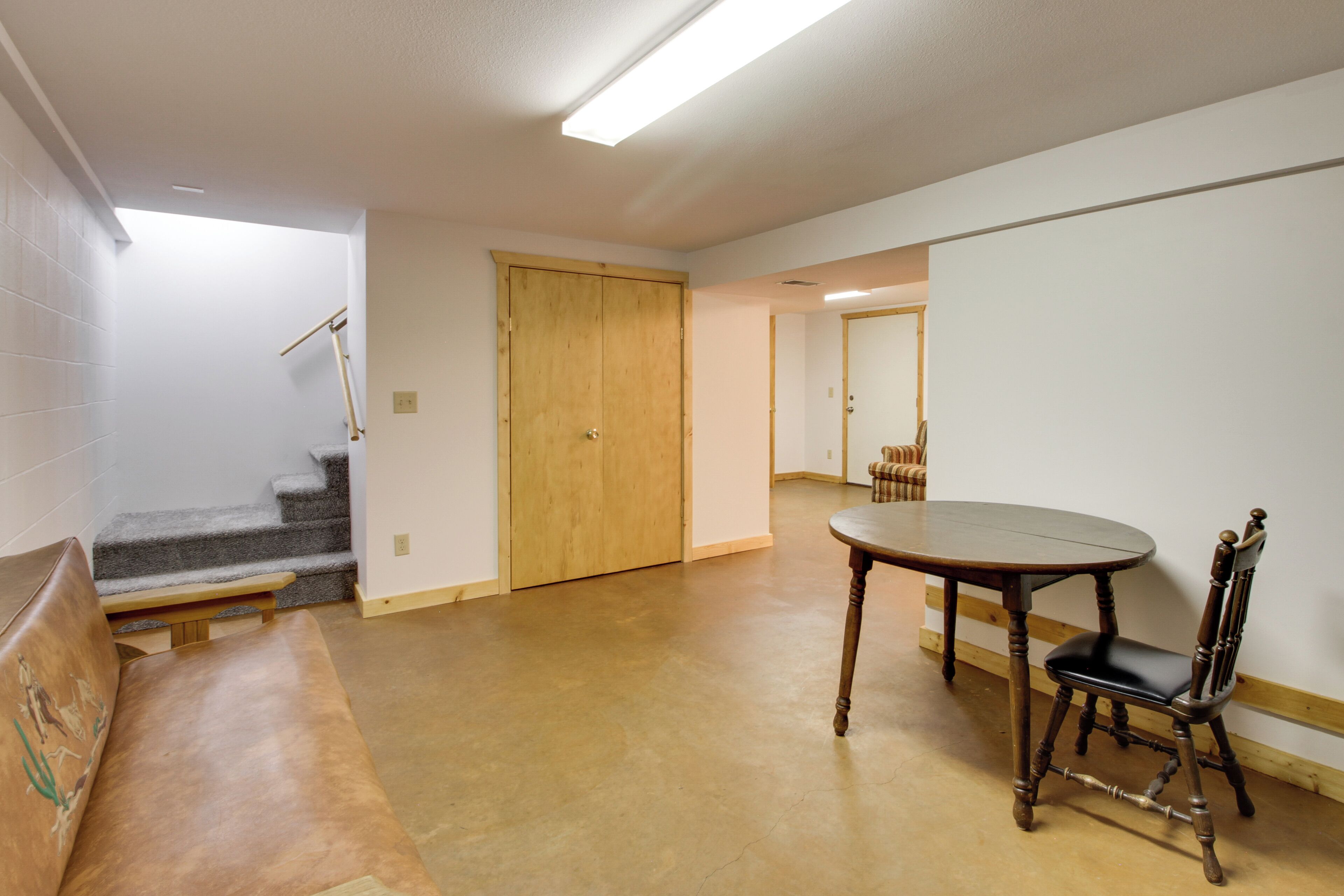 A room with a wooden table and chair, a bench, a door, and a staircase.