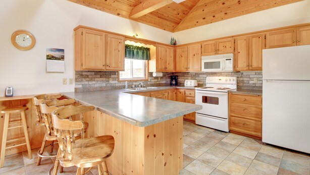A kitchen with wooden cabinets, a large island with bar stools, a microwave, stove, and a refrigerator. - Minnesota Cabin Rental: 3 Mi to Pelican Lake! (Pequot Lakes)