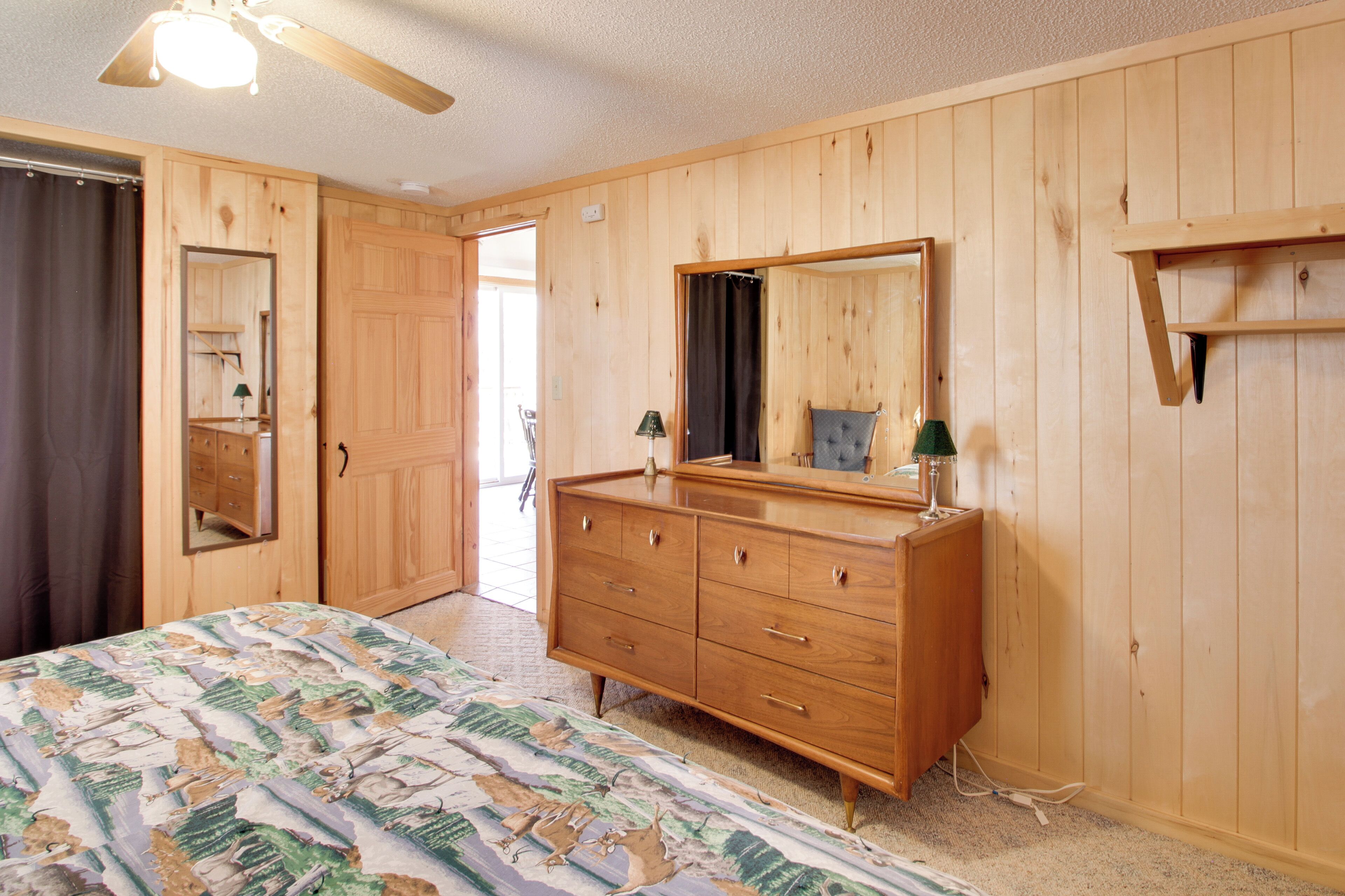 A wooden-paneled room with a bed, dresser, and mirror.