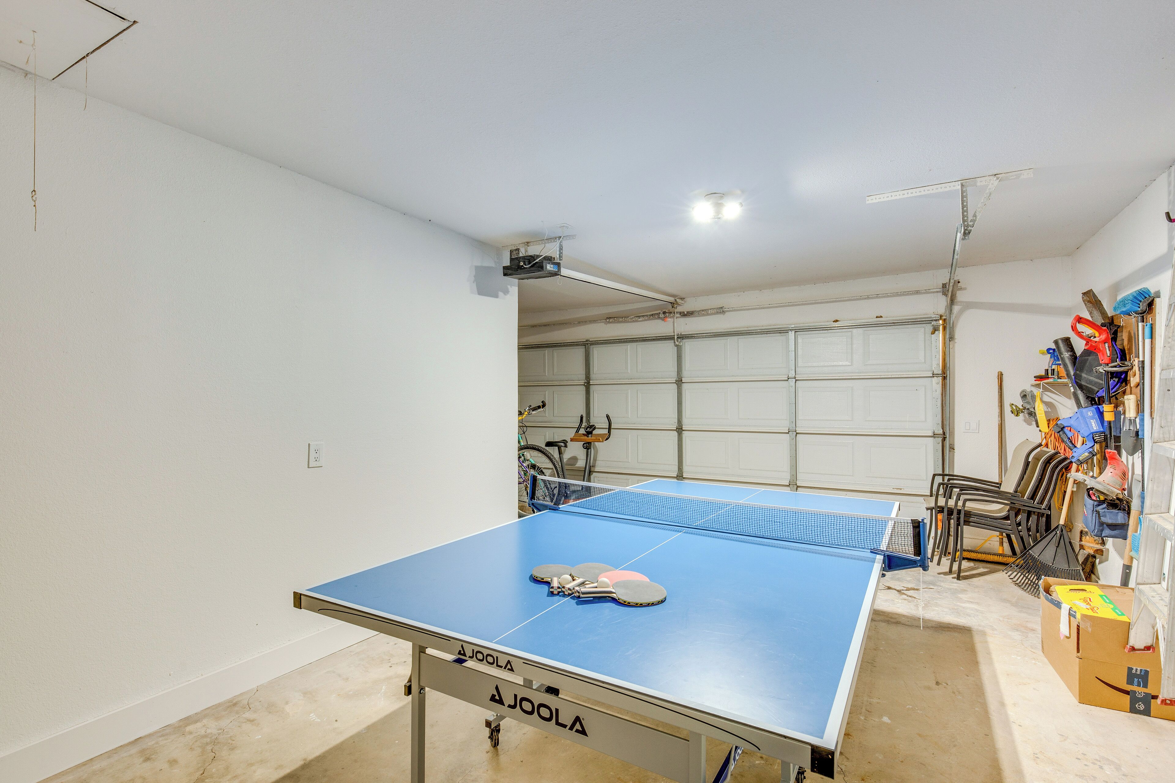 A ping pong table with paddles, a bicycle, and a garage door in the background.