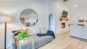 Un salon moderne avec un canapé gris, un miroir rond, une lampe sur pied et une cheminée.