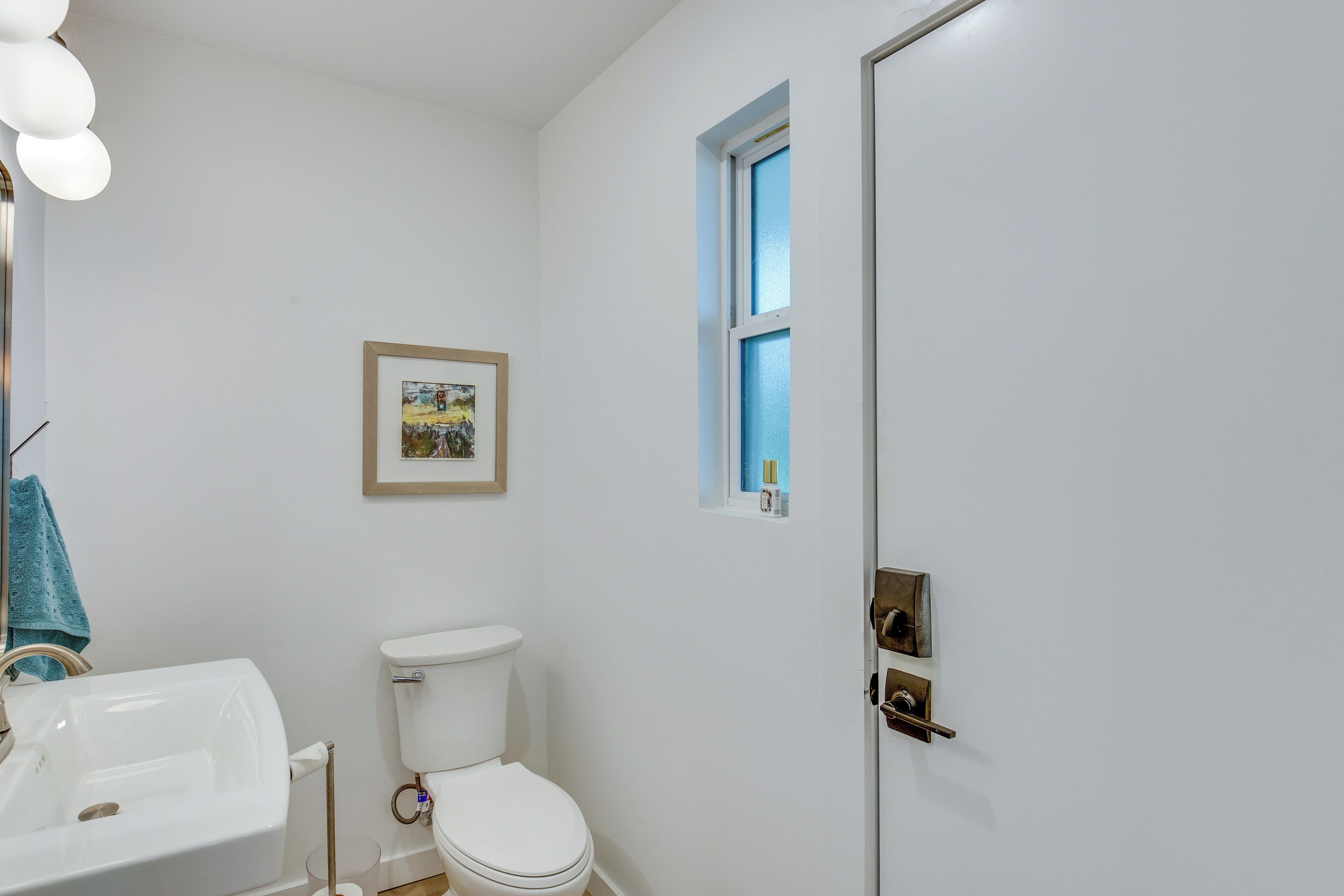 A bathroom with a white sink, toilet, and a framed picture on the wall.