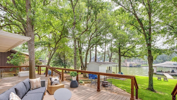 Une terrasse en bois avec des meubles d’extérieur, une vue sur une rivière et un petit abri de jardin en arrière-plan.