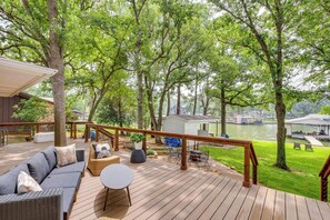 A wooden deck with outdoor furniture, a view of a river, and a small shed in the background. - Private Dock: Lakefront Enchanted Oaks Retreat (Mabank)