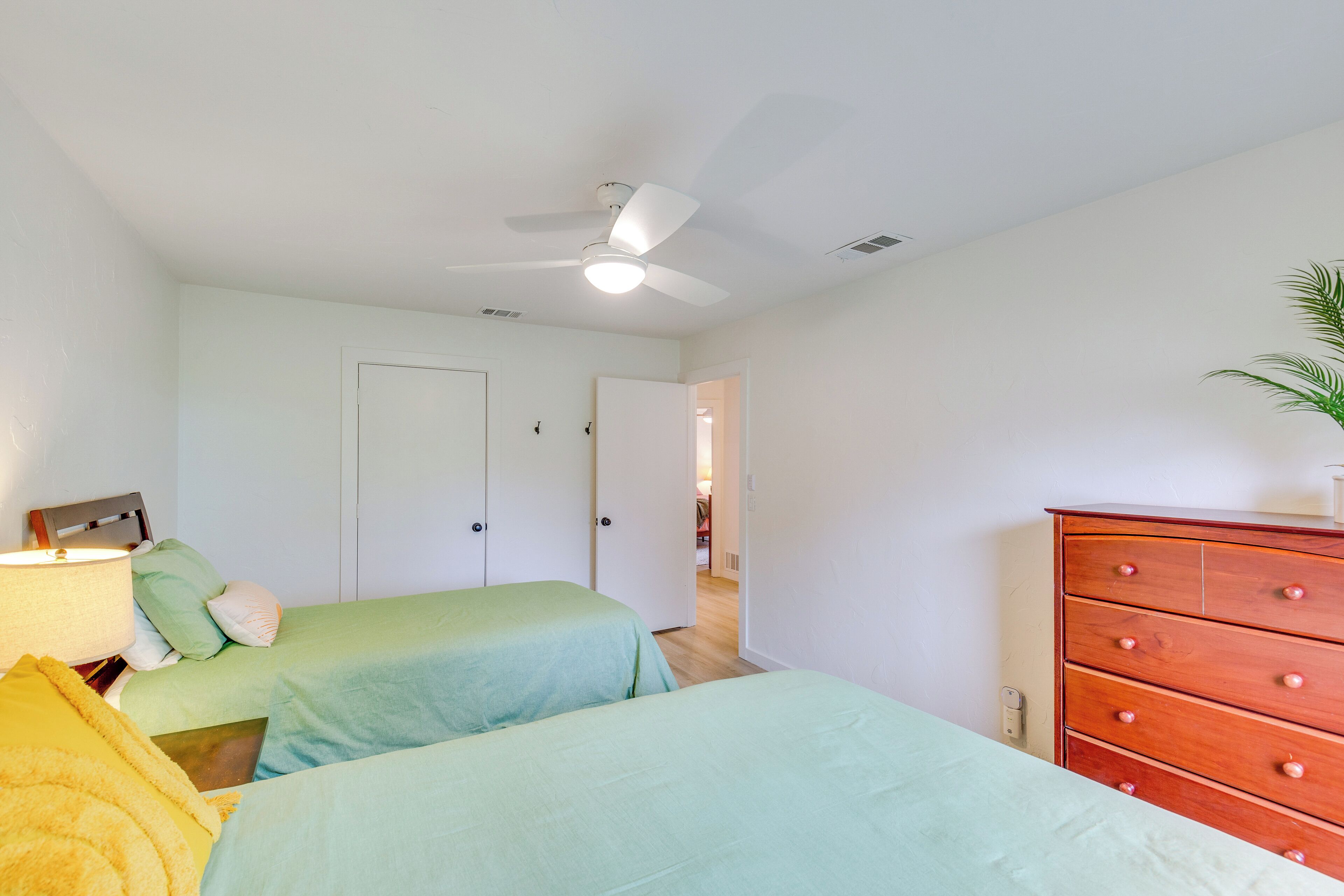 A bedroom with two beds, a ceiling fan, a wooden dresser, and a lamp.
