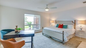Une chambre à coucher comprenant un lit, des lampes de chevet, un ventilateur de plafond, une fenêtre et une table à manger avec des chaises.
