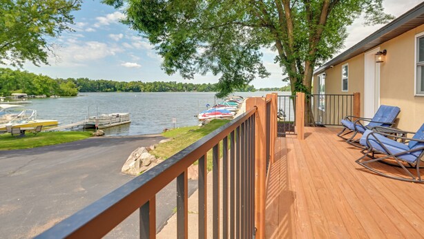 A wooden deck with blue chairs, a view of a lake, boats docked, and trees. - Chippewa Falls Getaway w/ Community Lake Access! (Chippewa Falls)