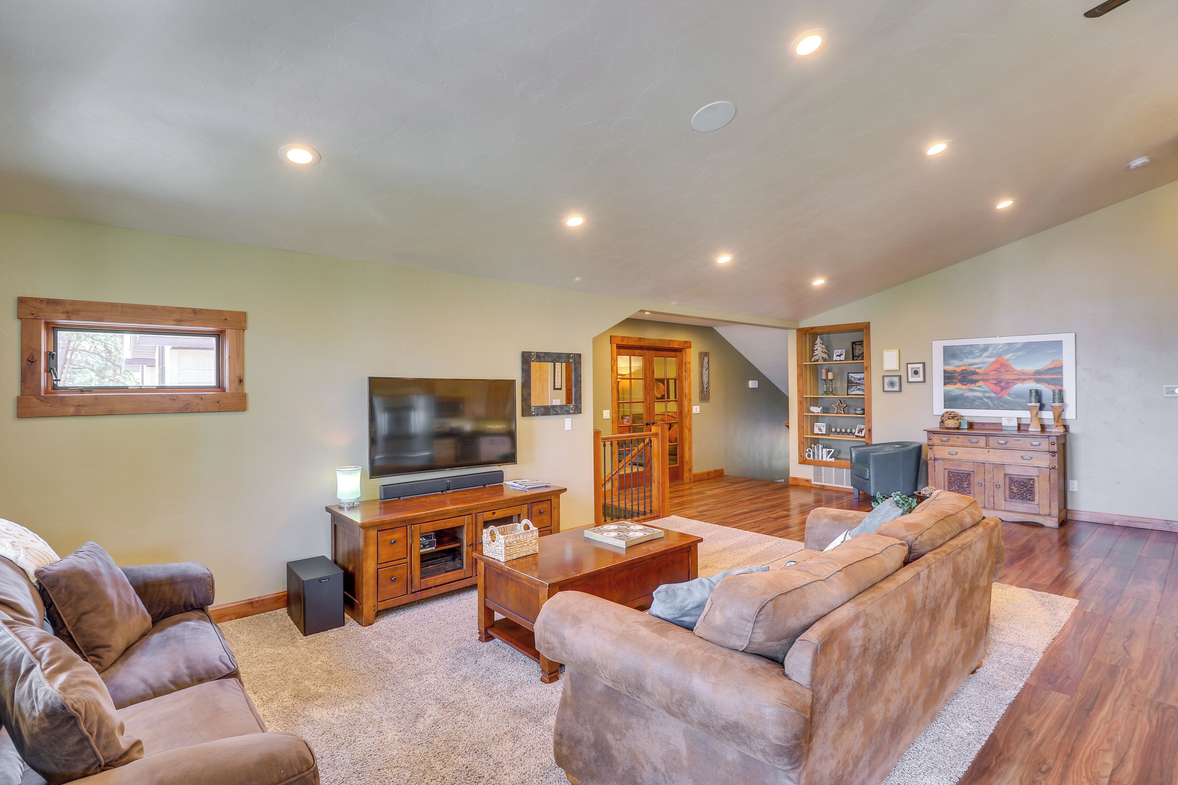 A spacious living room with a large flat-screen TV, leather sofas, a wooden entertainment center, and a staircase leading to an upper level.