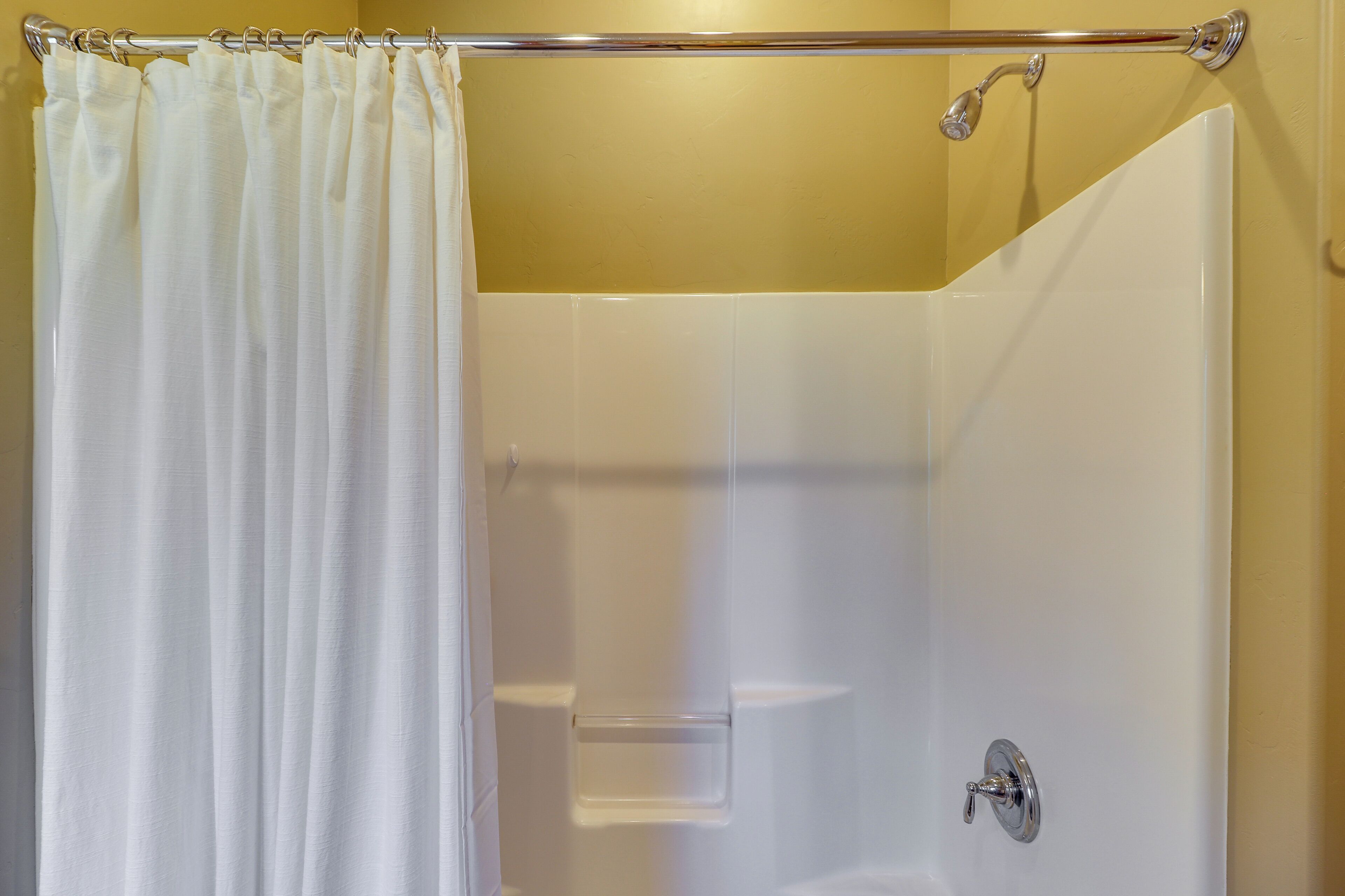 A shower area with a white curtain, a glass door, and a chrome showerhead.