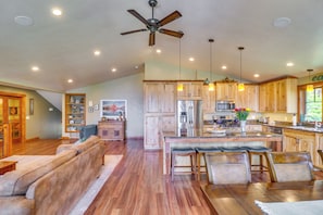 A spacious living area with a wooden floor, a ceiling fan, and a kitchen with wooden cabinets and stainless steel appliances. - Flathead Lake Base Camp in Somers: Lake View! (Somers)