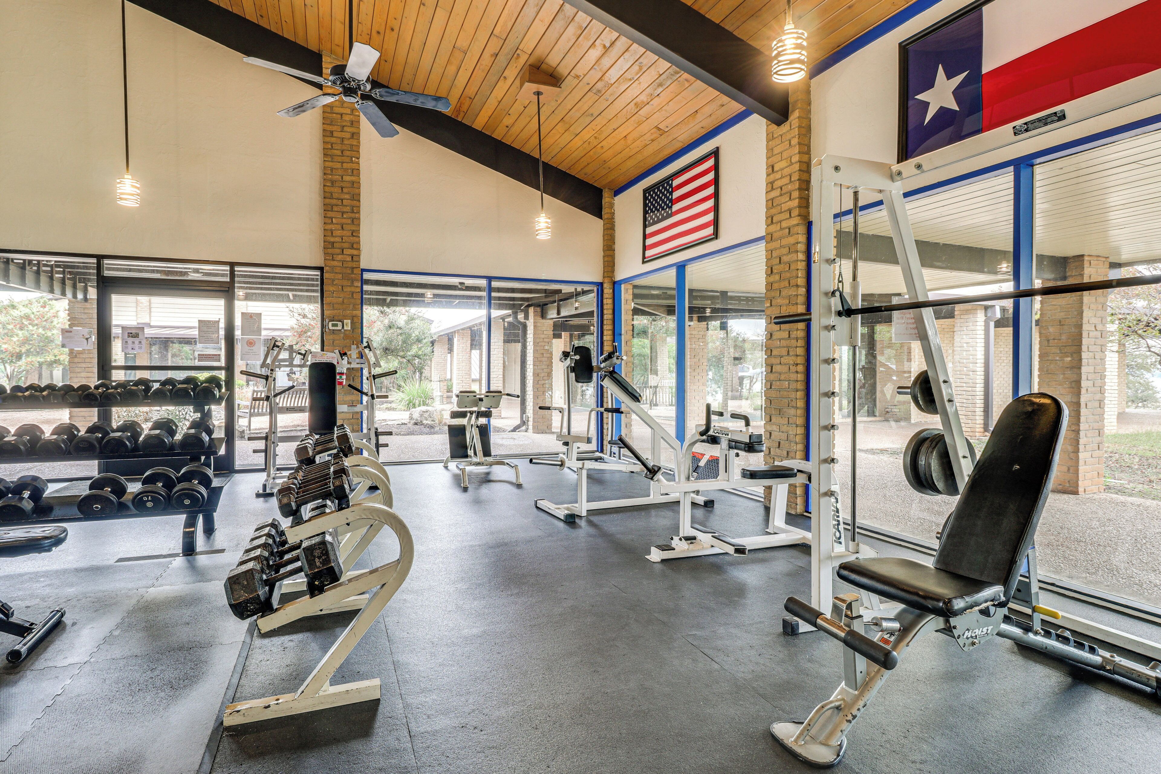 A gym with various exercise equipment, a Texas flag, and a view of the outside.