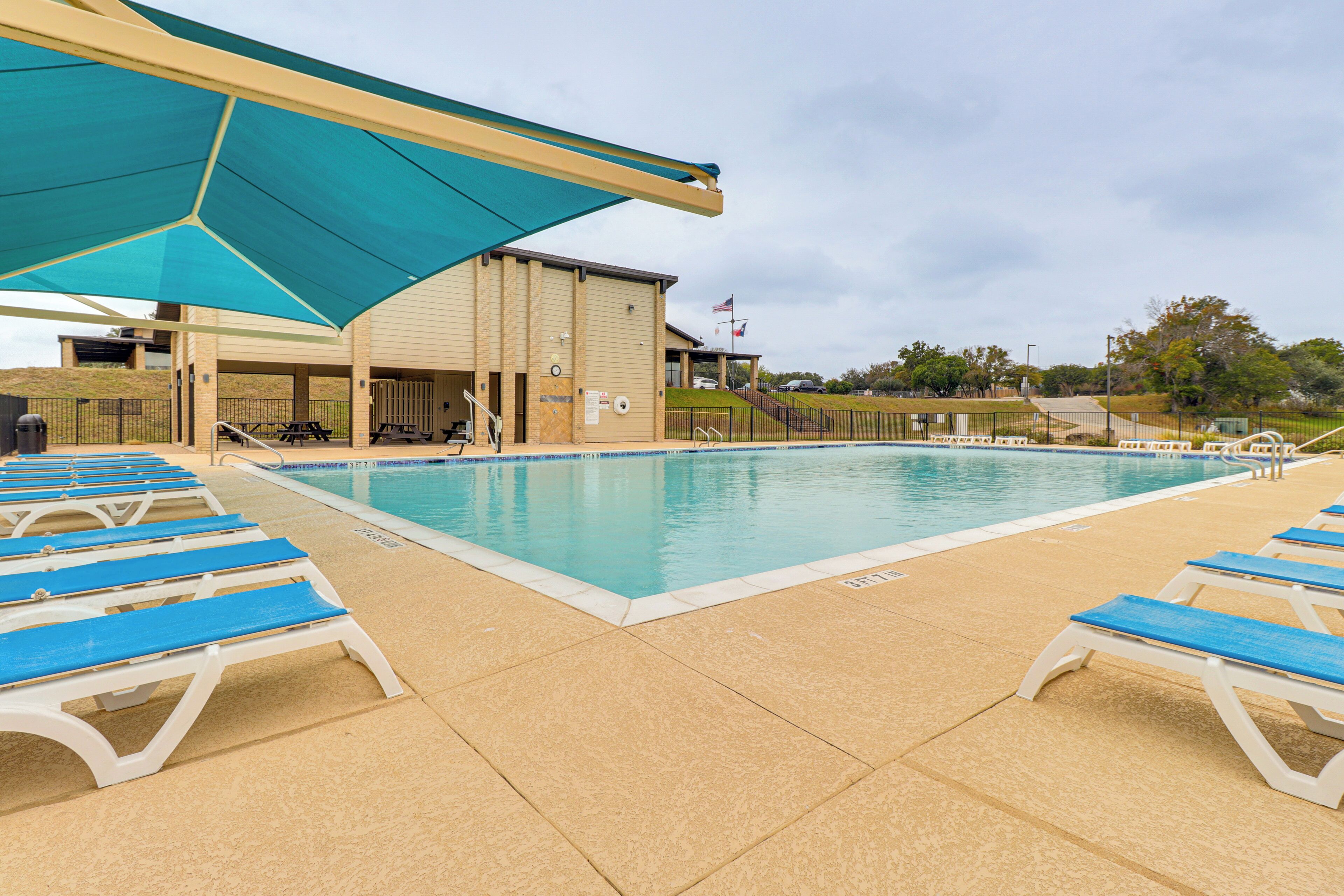 Une piscine avec des chaises longues bleues et un espace ombragé.