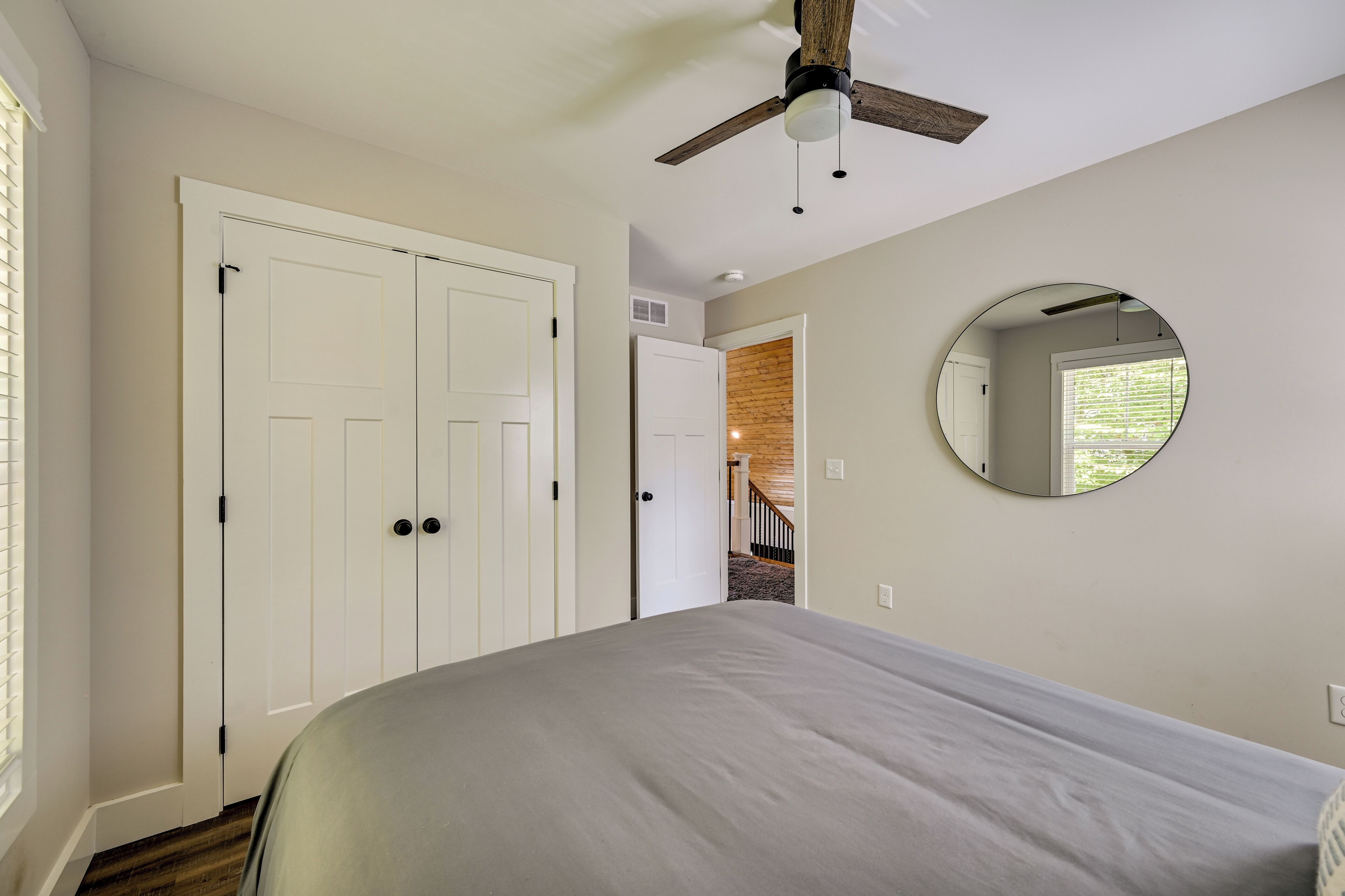 A bedroom with a bed, a ceiling fan, a large mirror, and a closet.