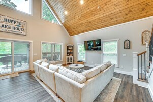 A spacious living room with a large sectional sofa, a wooden ceiling, and a TV mounted on the wall.